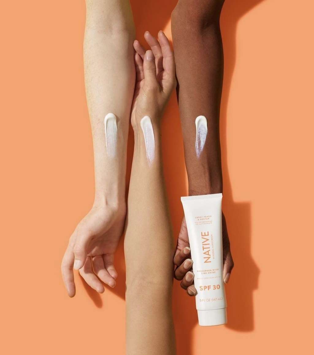 Three arms with different skin tones show sunscreen application next to a tube of Native SPF 30 against an orange background.