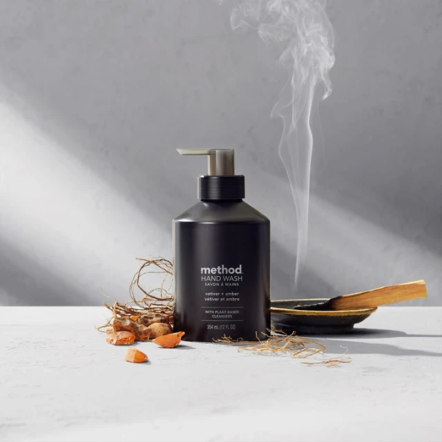 Close-up of a Method brand hand wash bottle with aromatherapy elements, smoke, and warm lighting on a bright surface.