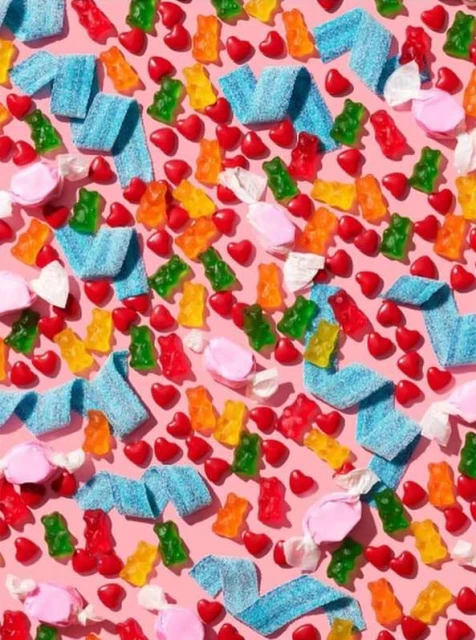 Overhead shot of colorful candy including gummy bears, sour belts, and heart-shaped candies arranged on a pink surface.