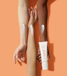 Three arms with different skin tones displaying dollops of white sunscreen against an orange background