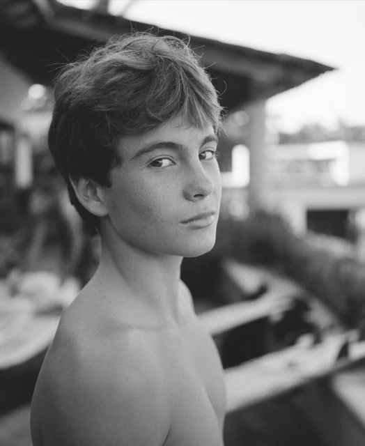 Black and white portrait of a young adult with medium length hair, looking at the camera. Outdoor setting with blurred background.