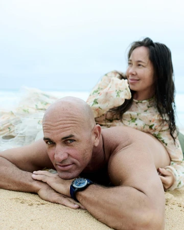 Portrait of a man lying on a sandy beach with a woman seated behind him, captured by Anne Menke