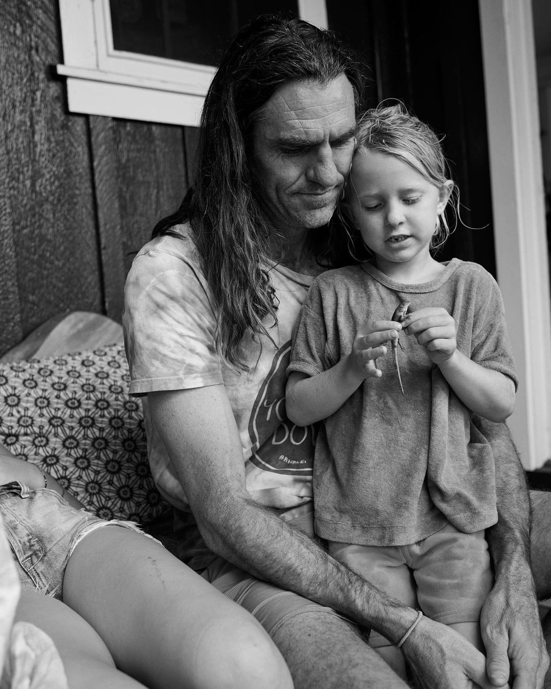 Monochromatic portrait of a father and young child sitting on a porch, with an additional person partially visible to the side.
