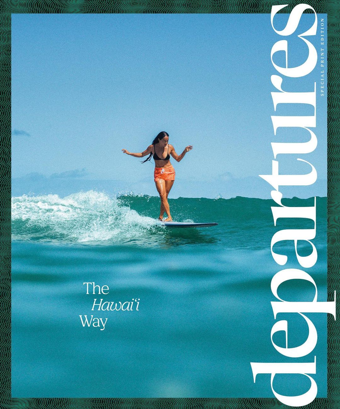 An athletic female surfer rides a wave on a longboard under a clear blue sky, framed by a green border featuring a magazine cover.