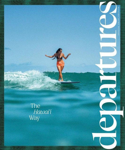 An athletic female surfer rides a wave on a longboard under a clear blue sky, framed by a green border featuring a magazine cover.