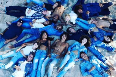 Group of diverse models wearing denim and white shirts lying in a circle on sandy beach