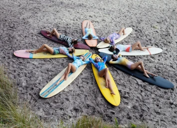 Aerial view of seven women lying on surfboards arranged in a circle on sandy beach