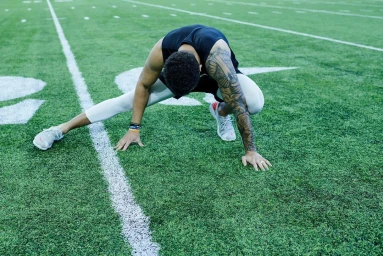 An athlete stretching on a green artificial turf sports field marked with white yard lines.