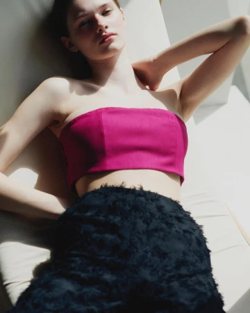Model in magenta strapless top and textured black skirt lying against light background by Anne Pique