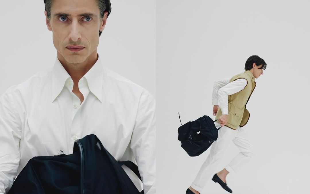 An adult male model presents fashion items, including a white shirt and black backpack, in a studio setting with a clean white backdrop.