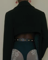 Rear view of a person wearing a cropped black jacket, studded leather belt, and patterned tights by photographer Anne Piqué.