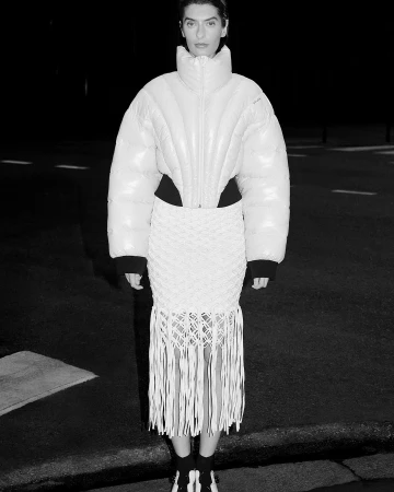 Model in a high-collared quilted puffer jacket and fringed skirt photographed at night by Anne-Sophie Soudoplatoff.