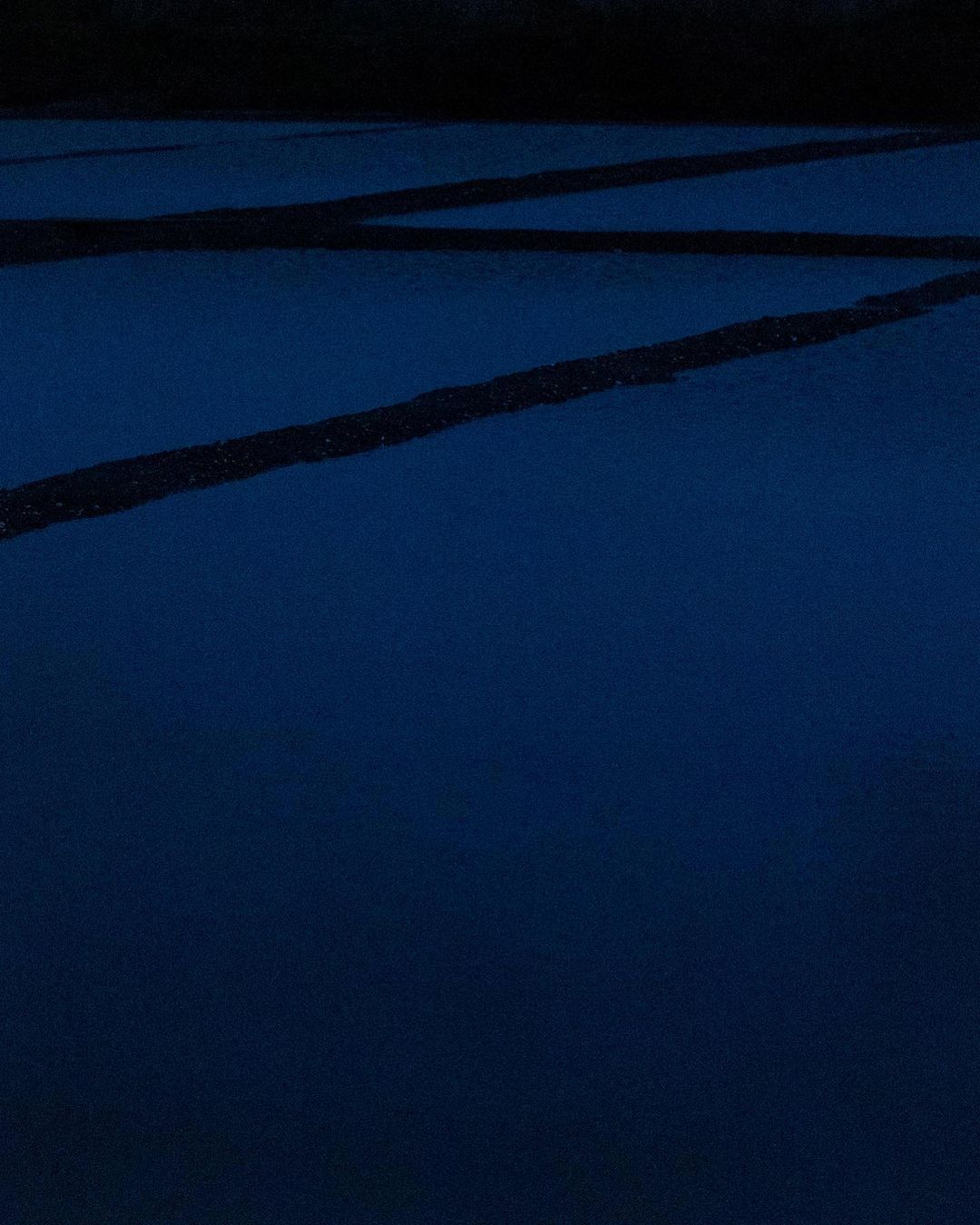 Minimalist abstract: Dark blue surface with parallel black lines crossing diagonally, creating geometric and linear patterns.