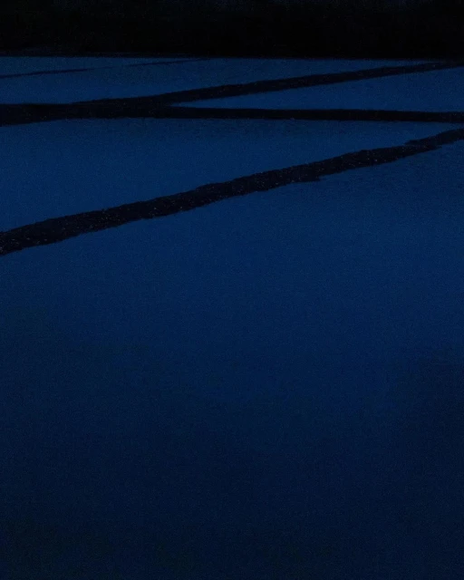 Minimalist abstract: Dark blue surface with parallel black lines crossing diagonally, creating geometric and linear patterns.
