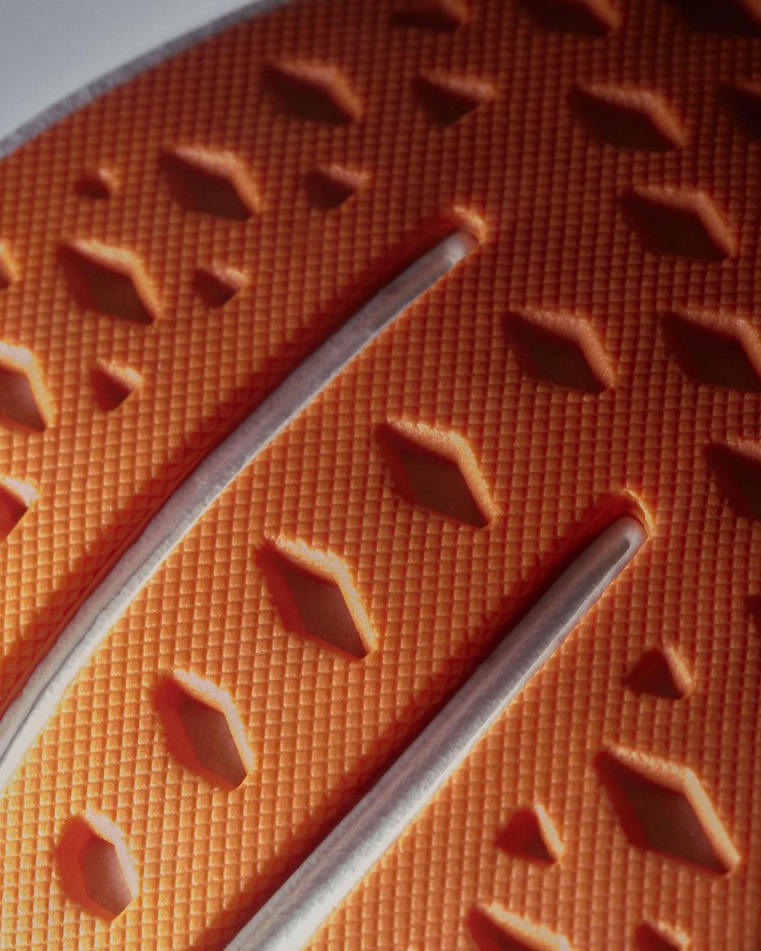 Close-up of an orange textured surface with diamond-shaped cutouts and grey grooves running across, creating an abstract pattern.