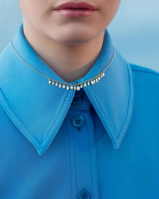 Close-up of a woman wearing a turquoise blue collared shirt and a dainty gold necklace with small gem pendants. Fashion shot.