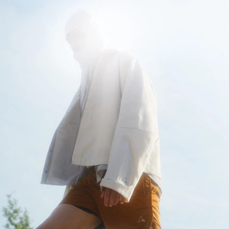 Low-angle shot of a model wearing a white jacket and brown shorts against a bright sky background.