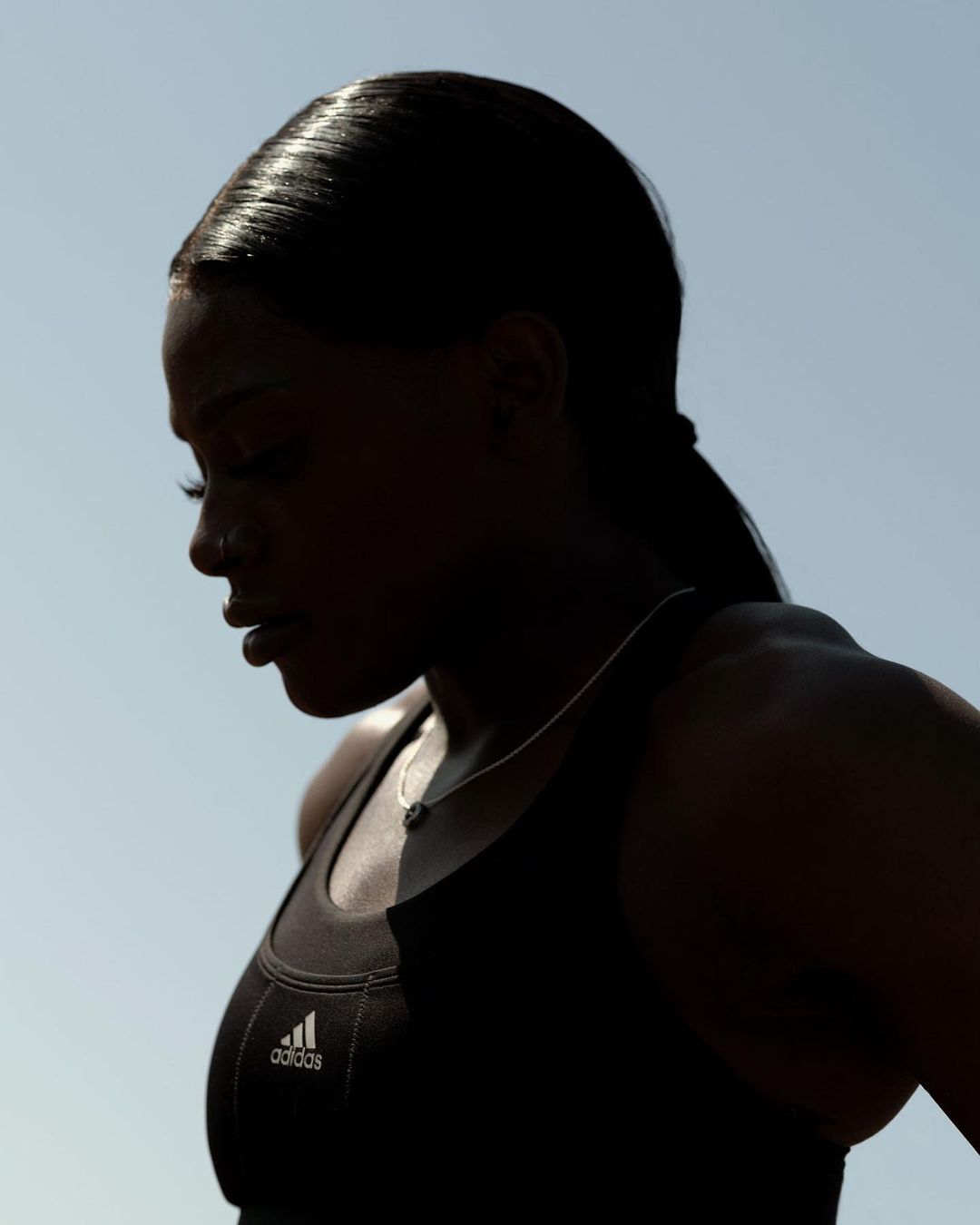 Silhouette of a Black female athlete in athletic wear against a blue sky, showcasing sportswear and athletic physique.