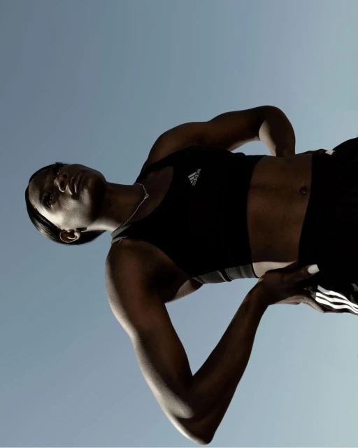 An athlete in sportswear with the Adidas logo poses in a low-angle shot against a bright blue sky, showcasing fitness and athletic apparel.