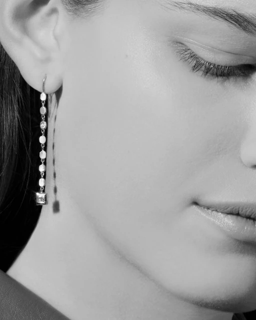 Close-up shot of a fair-skinned woman with an earring, showcasing the earring's design and texture against a blurred, neutral background.