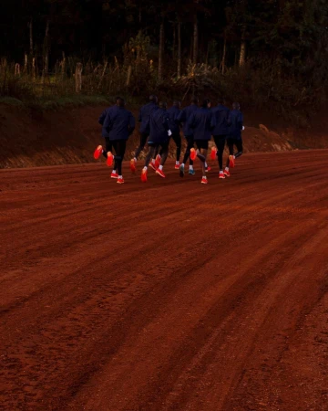 Group of runners in dark jackets and bright red running shoes running away on a red dirt road