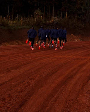 Group of runners in dark jackets and bright red running shoes running away on a red dirt road