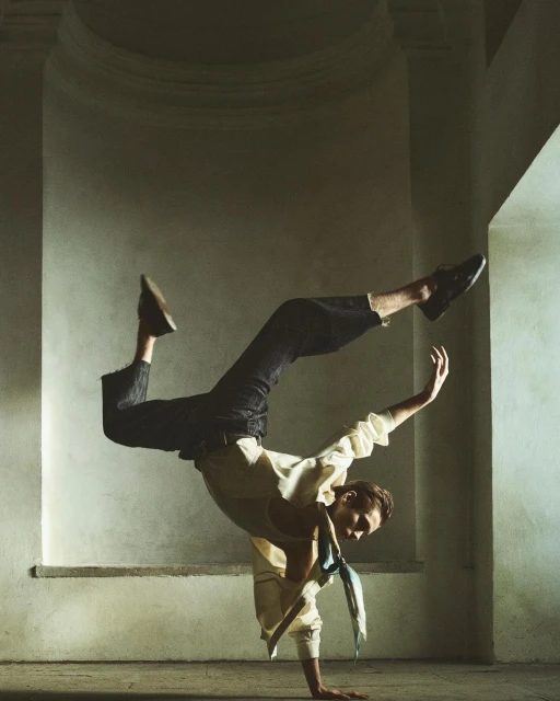 A person is doing a handstand in an arched hallway. They are wearing dress shoes, dark pants and a light colored shirt with a dark tie.
