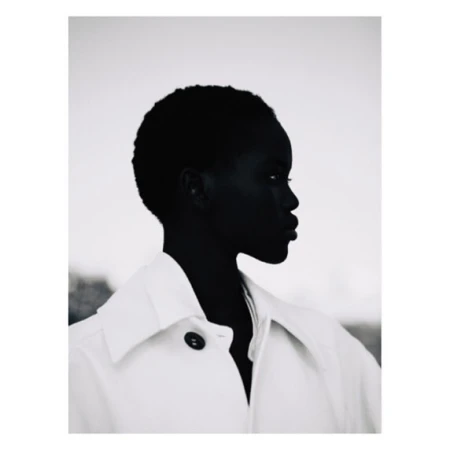 Monochromatic portrait of a dark-skinned woman in profile, wearing a white jacket against a neutral background, showcasing fashion and beauty.