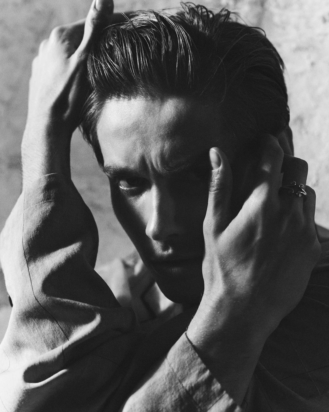 Close-up monochrome portrait of a man touching his hair and face by Annemarieke Van Drimmelen