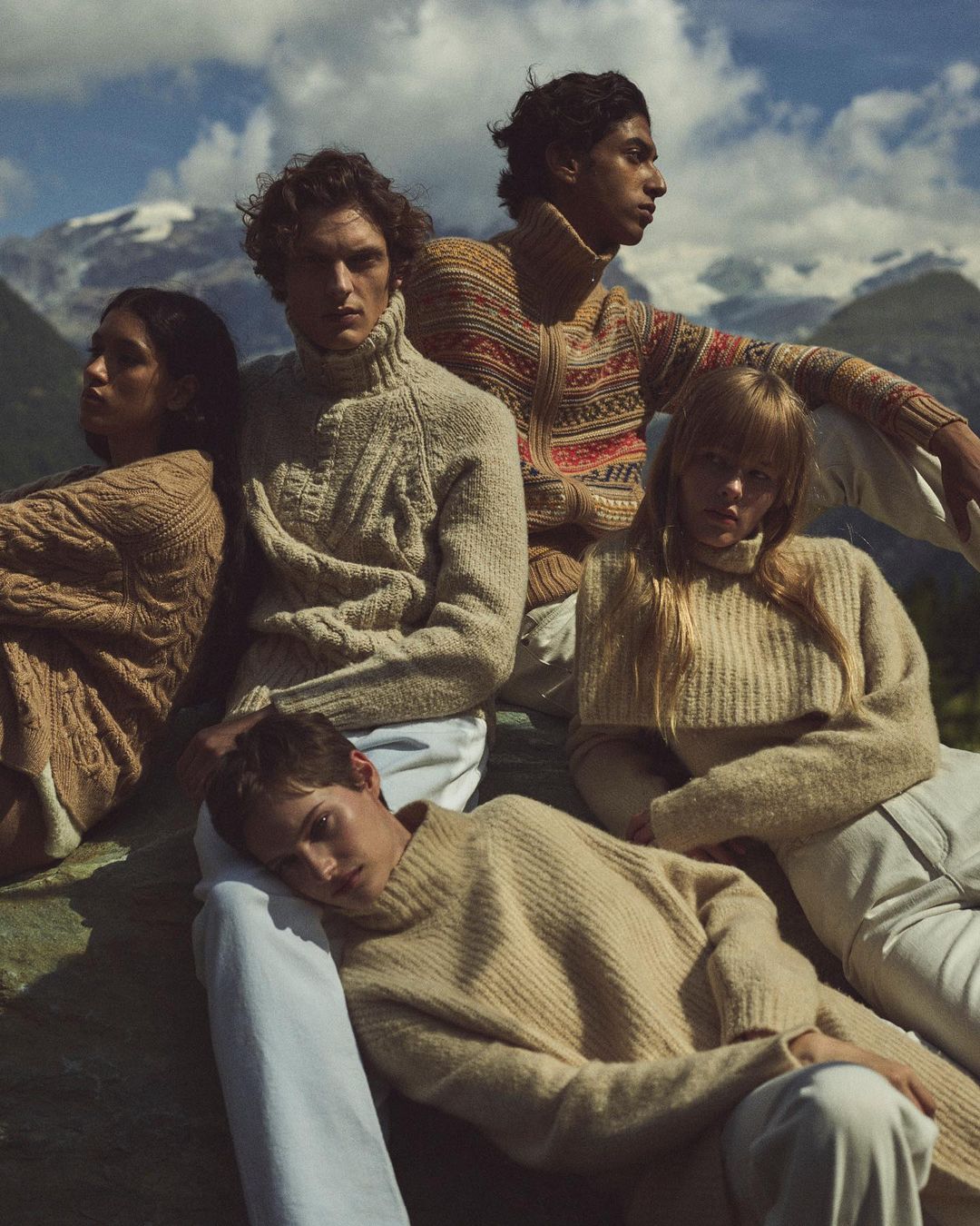 Group of five fashion models in outdoor mountain setting wearing knit sweaters and white pants in fashion editorial photography.
