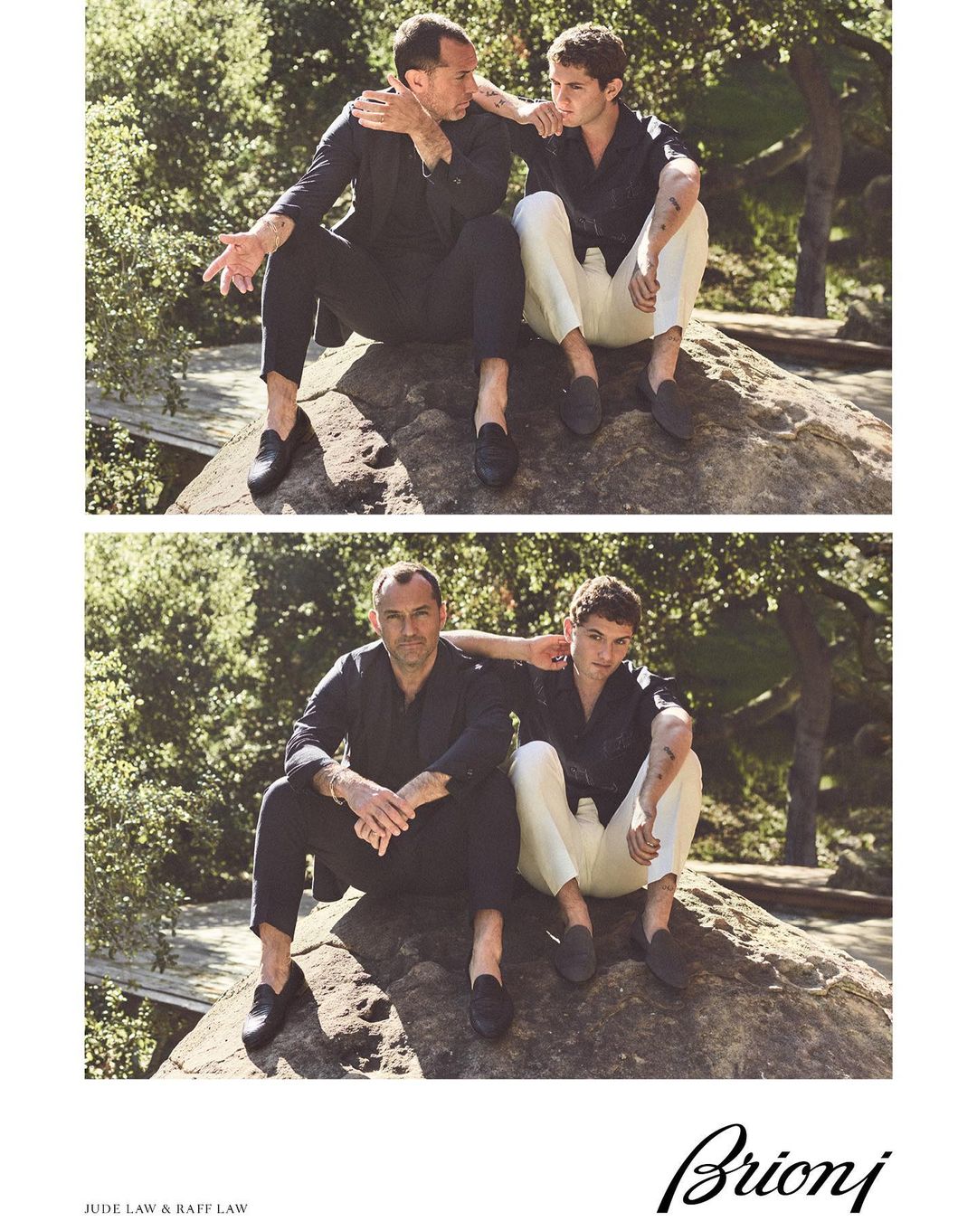 Two men seated on a rock in an outdoor setting, modeling menswear. One man wears a navy suit, the other wears white pants and a navy shirt.