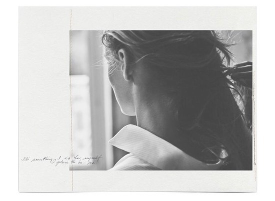 Monochromatic portrait of a person with long hair turned away from the camera, wearing a collared shirt and looking out of a window.