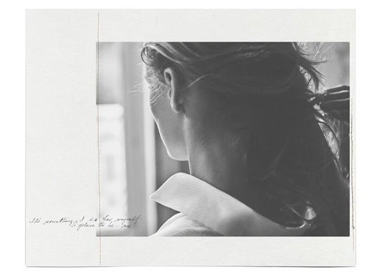Monochromatic portrait of a person with long hair turned away from the camera, wearing a collared shirt and looking out of a window.