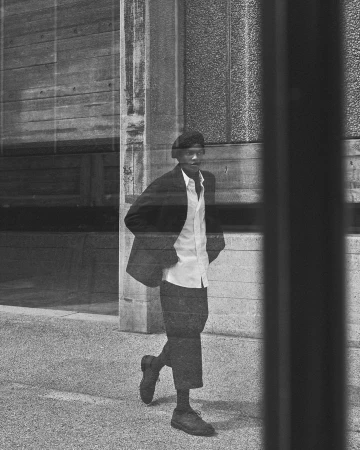 Black and white photo of an African American man in a suit walking on a city street, viewed through metal bars, creating a slightly distorted effect.