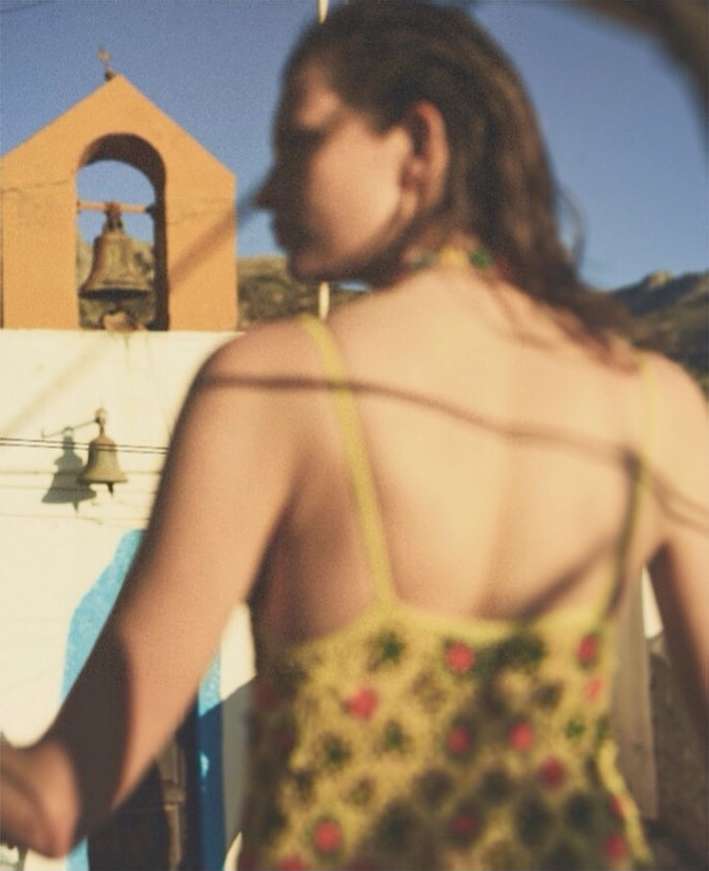 Woman in patterned sundress outdoors with yellow bell tower and mountain backdrop. Relaxing on a summer vacation.
