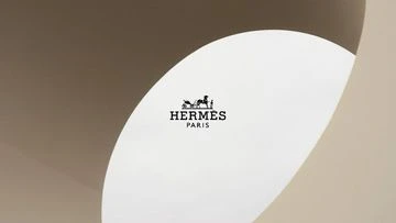 Minimalist composition with a white oval shape in a beige setting, featuring the 'HERMES PARIS' logo in black. Clean design.