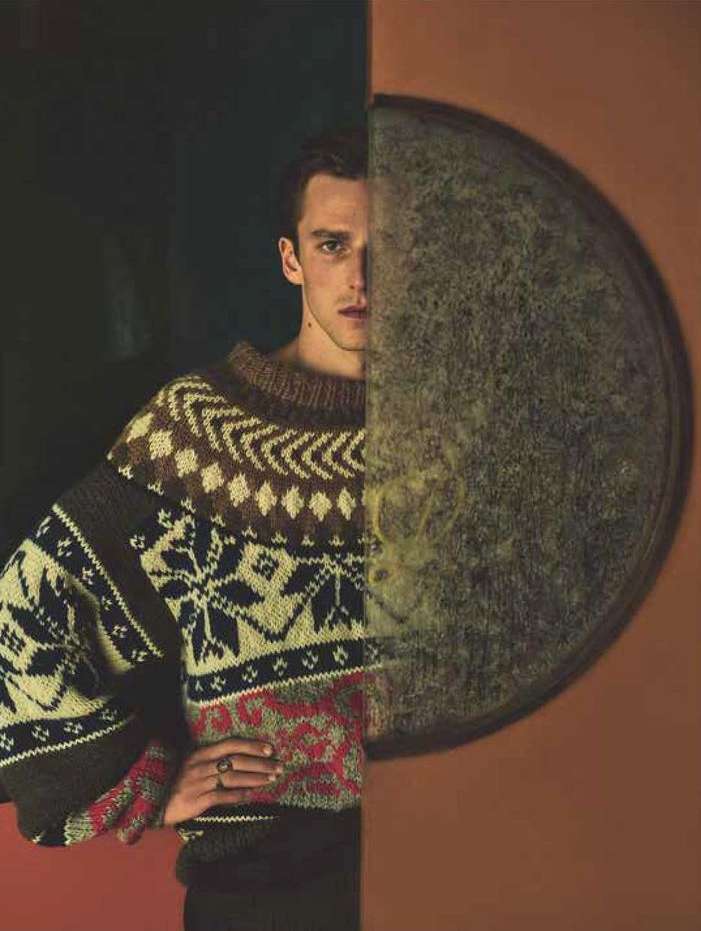 Portrait of a handsome adult male wearing a patterned sweater against a split background with a circle element and warm lighting.