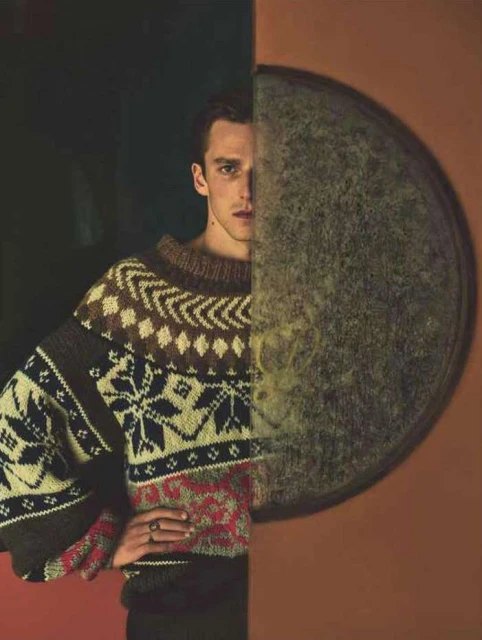 Portrait of a handsome adult male wearing a patterned sweater against a split background with a circle element and warm lighting.