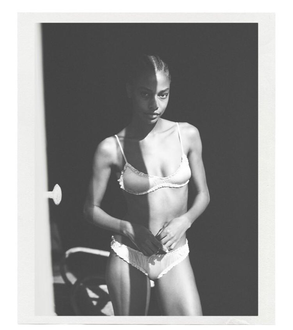 Monochrome studio portrait of a woman in lingerie with dramatic shadows, black background, and doorframe in the frame.