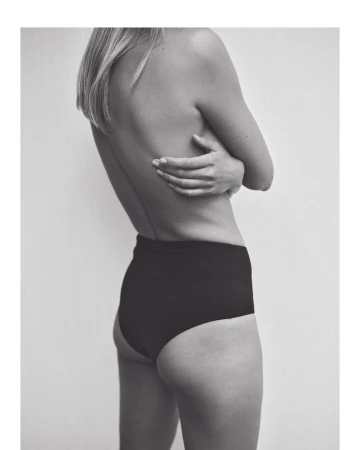 Back view of a fair-skinned adult female wearing black high-waisted bottoms, facing away from the camera with arms crossed.