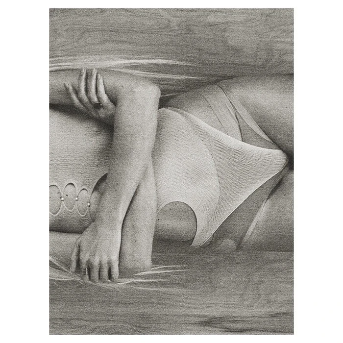 Monochrome close-up portrait of a woman lying down wearing a textured one-piece swimsuit against a wood grain background