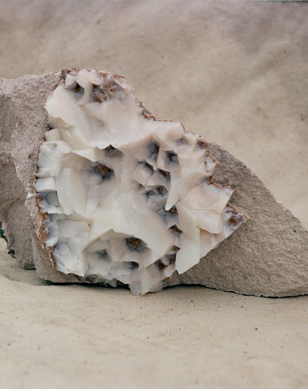Close-up of a white calcite mineral specimen featuring a crystal structure set against a grey, textured stone and neutral backdrop.