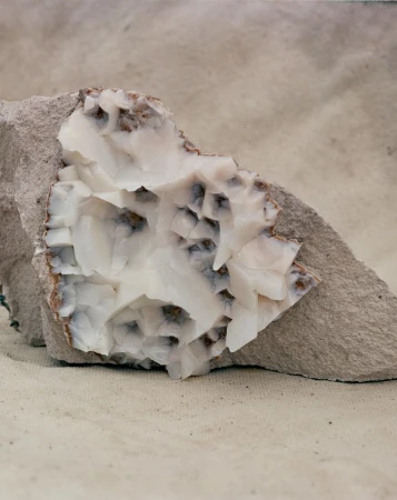 Close-up of a white calcite mineral specimen featuring a crystal structure set against a grey, textured stone and neutral backdrop.