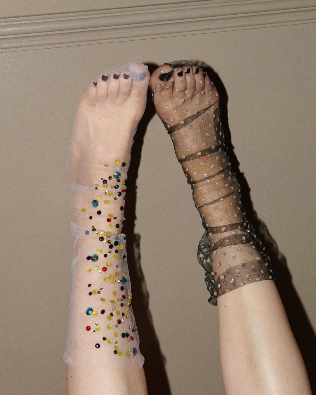 Two human legs wearing polka-dot socks and leg decorations against a neutral wall, showcasing fashion footwear design with textures.