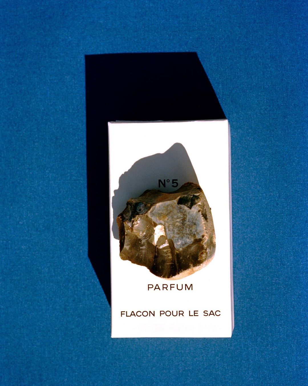 Still life shot of a rock placed on a white container with black text, all set against a saturated dark blue background.