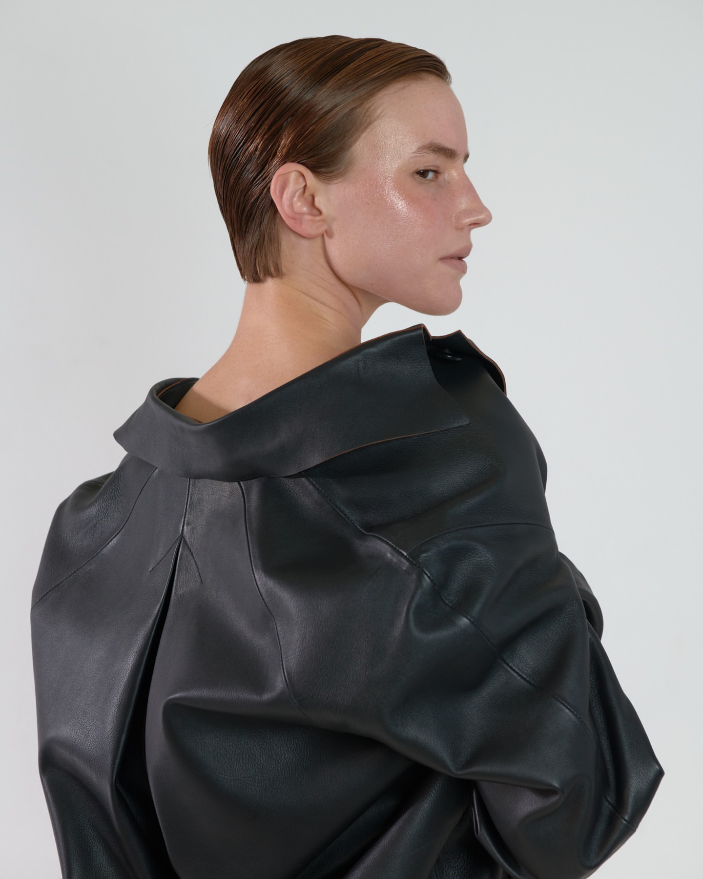 Woman with short hair wearing a black leather jacket posing in front of a neutral background in a studio-lit fashion editorial shot.