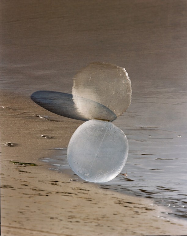 Balanced arrangement of three translucent stone spheres on a sandy beach with gentle waves lapping, creating a zen-like composition.