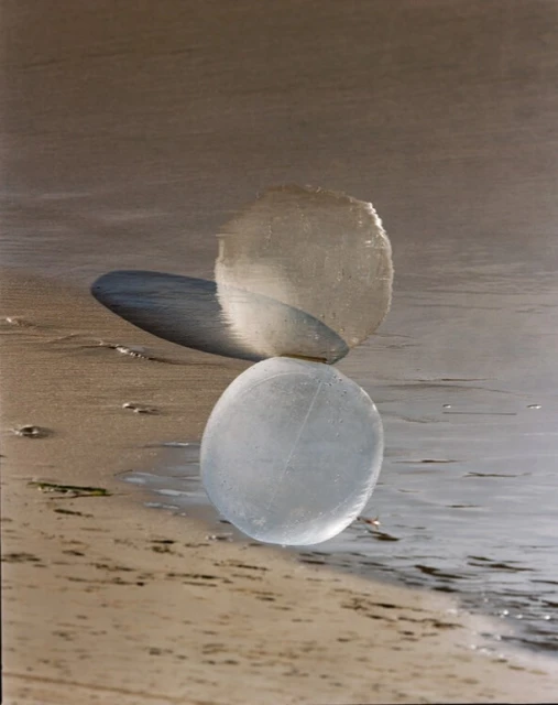 Balanced arrangement of three translucent stone spheres on a sandy beach with gentle waves lapping, creating a zen-like composition.