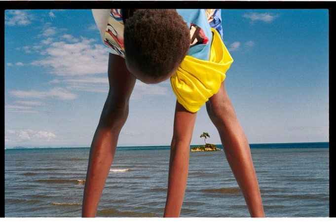 Child stands on a beach with an island in the distance on a clear day. View is slightly tilted upward.
