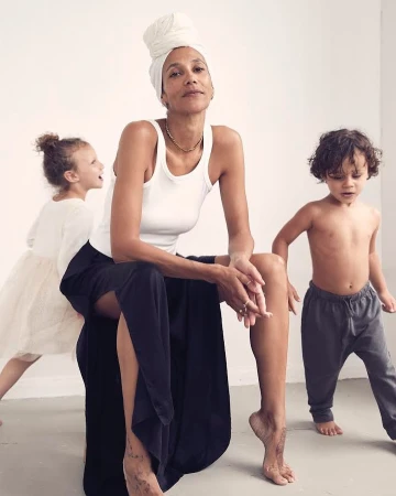 Woman in white tank top and turban seated with two children in a minimalist studio setting by Annie Bundfuss